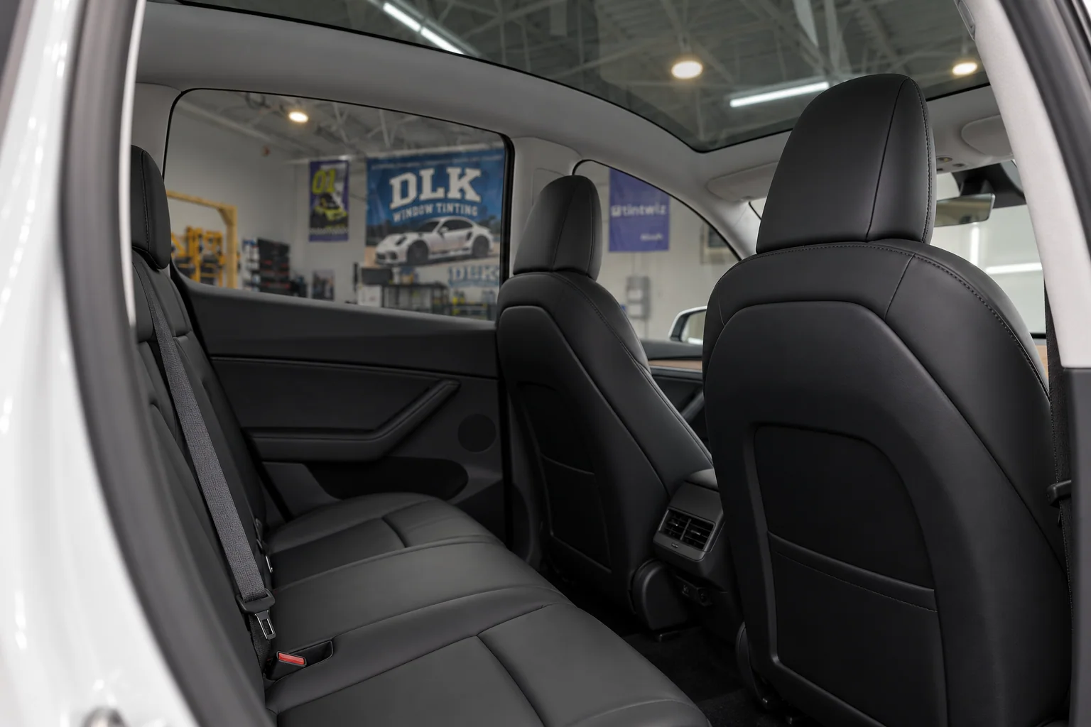 Black Tesla seats and panoramic glass with the DLK workshop visible through the tinted side window
