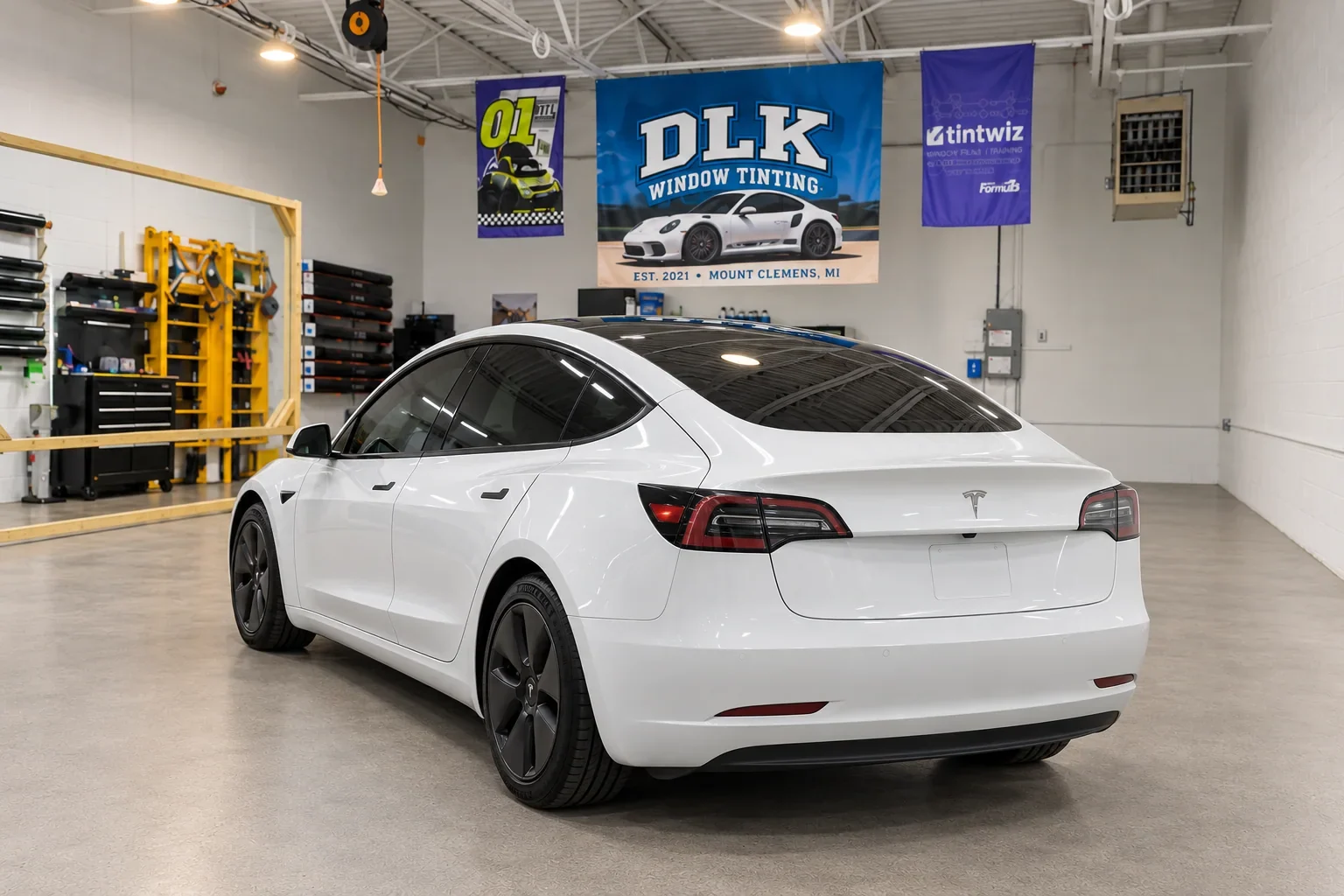 Rear three-quarter view of a white Tesla with dark tinted glass inside the DLK workshop