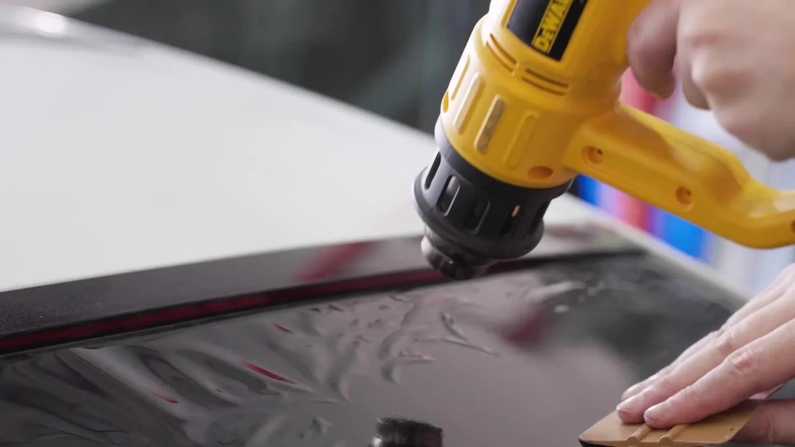Installer shrinking window film to a car window with a heat gun